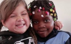 dos estudiantes de educación básica de diferente nacionalidad abrazándose y sonriendo a la cámara.