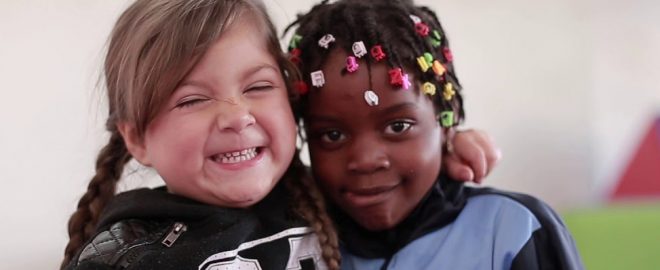 dos estudiantes de educación básica de diferente nacionalidad abrazándose y sonriendo a la cámara.